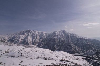 Güneşli bir günde açık mavi bir gökyüzünün altında karla kaplı sıradağlar.
