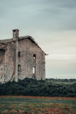 Kalın, koyu yeşil bir çitin arkasında pencereleri olmayan eski, taş bir ev duruyor..