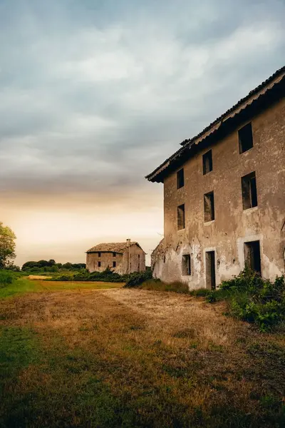 Terk edilmiş kırsal binalar, bulutlu gökyüzünün altında çimlerle çevrili.
