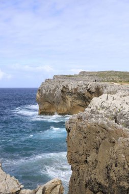 Dalgaların mavi gökyüzünün altında kayalıklara çarptığı Rocky kıyı manzarası