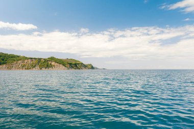 Gökyüzünün altındaki yeşil kıyı kayalıklarının yanında sakin okyanus dalgaları