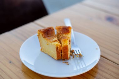 Tahta masadaki gümüş çatalla beyaz tabakta bir dilim cheesecake.