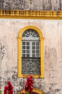 Architectural detail of colorful window set in weathered wall with blooming flowers