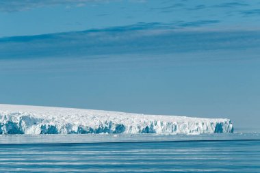 Buzdağı bulutlu gökyüzünün altında durgun mavi sularda yüzüyor.