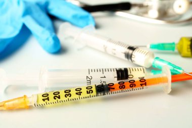 Arka planda mavi eldivenli, sarı sıvıyla dolu birden fazla şırınga ve şırınga yakın plan..