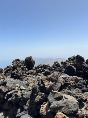 Açık mavi gökyüzünün altında uzak dağlarla kayalık bir manzara.
