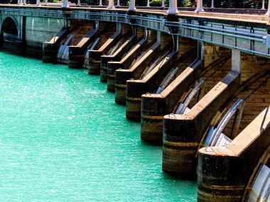Turkuaz su yüzeyi boyunca birden fazla sızıntı olan beton baraj yapısı