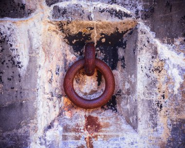 Paslı metal halka eskimiş beton duvara gömülmüş ve boyası soyulmuş.