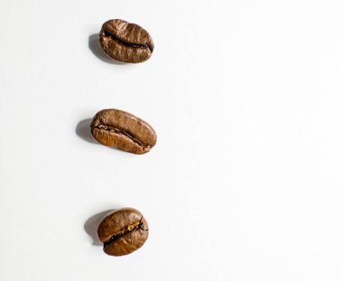 Beyaz arka planda dikey olarak dizilmiş üç kavrulmuş kahve çekirdeği.