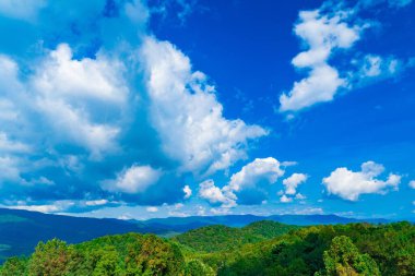 Parlak mavi gökyüzü dağların üzerinde kabarık beyaz bulutlarla dolu.
