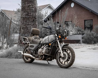 Evin yanında ağaçlar ve bitkilerle park edilmiş bir motosiklet.