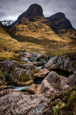 Sarp 'ın önünde dalgalanan Rocky Nehri, Bulutlu Gök altında Craggy Dağları olan Manzaralı Dağlar