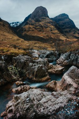 Sarp 'ın önünde dalgalanan Rocky Nehri, Bulutlu Gök altında Craggy Dağları olan Manzaralı Dağlar