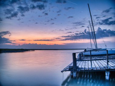 Sakin suların üzerinde sakin bir günbatımı limana yanaşmış yelkenliyle