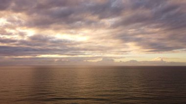 Gün batımında bulutlu gökyüzünün altında sakin okyanus dalgaları