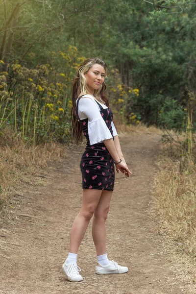晴れた日に森の真ん中の道に笑顔で立っているカジュアルなドレスと多色の髪の若い女性 — ストック写真
