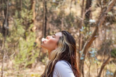 Güneşli bir günde arka planda odak ağaçlarından sakız çiğneyen genç beyaz bir kadının fotoğrafını çek..