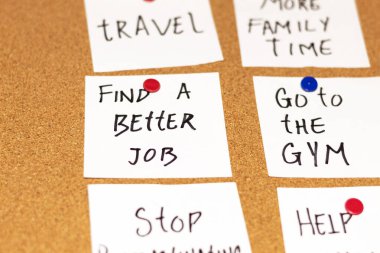 Close up of white post-it notes with new year's resolutions on a cork board. Texts: Find a better job and Go to the gym clipart