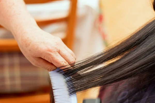 A stylist styling a woman\'s long black hair using a comb