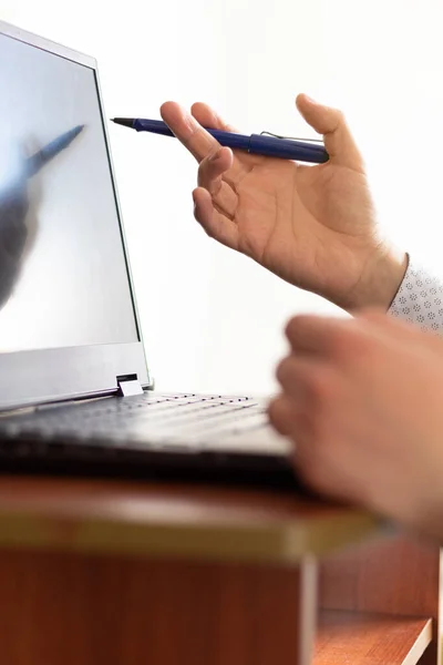 Close up on a man having a virtual meeting in front of his computer while moving his hands and holding a pen