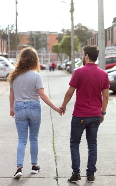 A heterosexual couple in love walking hand in hand on a street on a sunny day