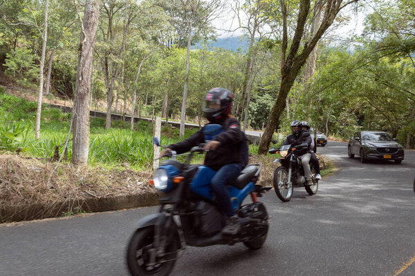 Antioquia, Colombia - July 29, 2022: Motorcyclists and cars in motion on a road surrounded by nature during a sunny day