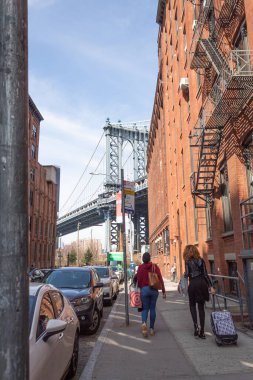 New York, Estados Unidos - March 26, 2022: Two unrecognizable women walking through Dumbo (New York) with the Manhattan Bridge in the background