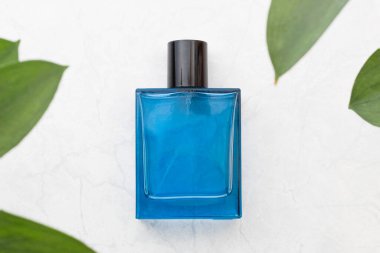 Ön planda yeşil yapraklar olan beyaz desenli mavi bir parfüm şişesi.