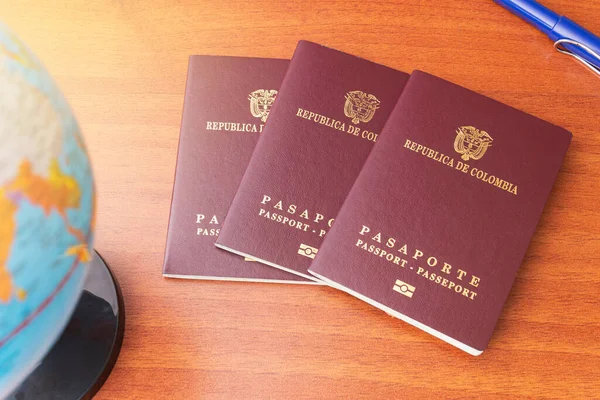 Üç Kolombiya pasaportu bir küre ve tahta bir masanın üzerine yayılmış.