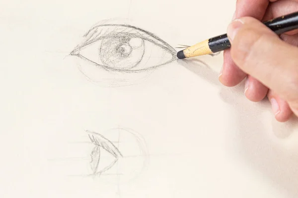 Close-up of an artist drawing an eye in two perspectives with a charcoal pencil in a sketchbook