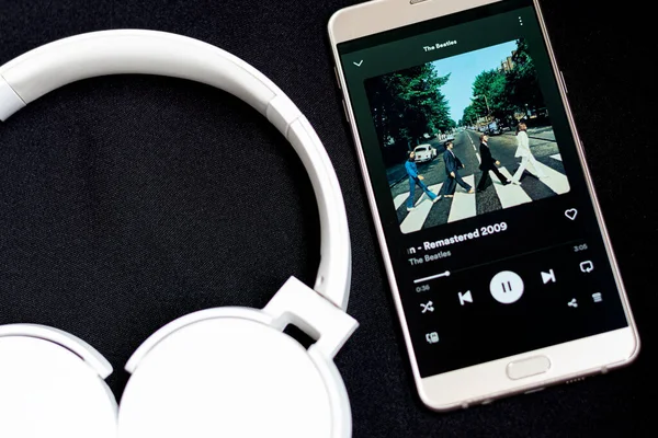 Bogota, Kolombiya - 26 Temmuz 2023. Beyaz kulaklıkların yanında The Beatles 'ın şarkısını çalan bir akıllı telefon. Müzik konsepti.