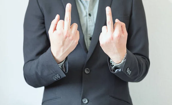 Unrecognizable businessman impolite and rude, showing the middle finger of his two hands in front of camera. Aggressive elegant man without tie in front of a plain background.