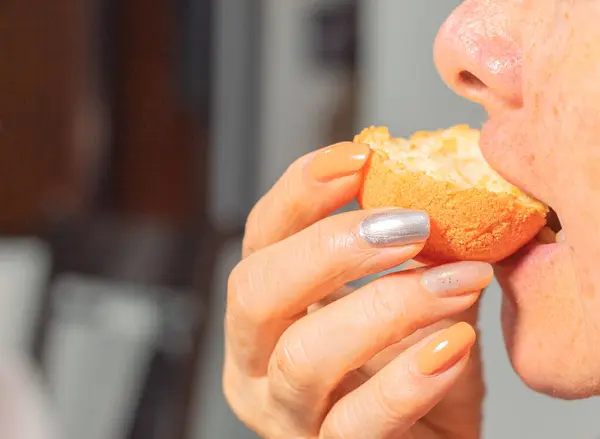 An unrecognizable woman with painted nails eating a Colombian fritter. Typical food concept. Breakfast. Colombian Bunuelo.