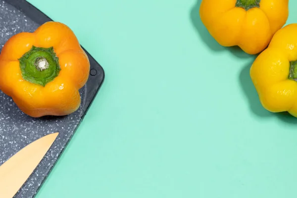 Food background. A yellow bell pepper on a cutting board next to a knife on an aquamarine background. Some fresh peppers.