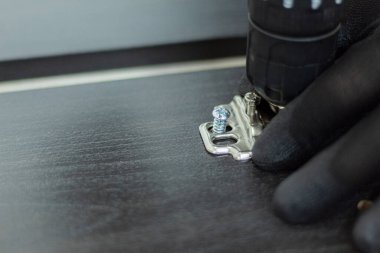 Bir insanın eline ahşap panele küçük bir menteşe yerleştirirken yakın çekim. İş aletleri. Ev yapımı marangozluk işi..