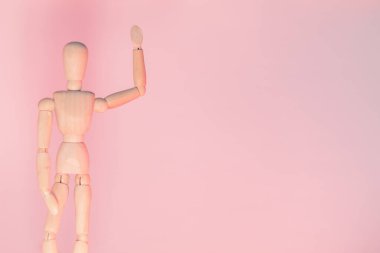 Bir eli pembe arka planda duran tahta çizim mankeni. Kopyalama alanı olan resim. Selamlama işareti.