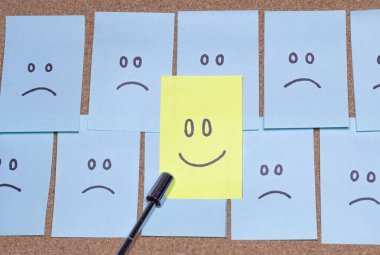 Mavi ofis notları, mantar panoya elle çizilmiş üzgün yüzler, mutlu yüzlü sarı bir not ve bir işaretçi tarafından işaret ediliyor..