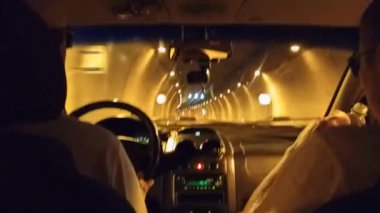 Metro tünelinden geçen bir arabada şoför ve yardımcı sürücü. İki tanınmayan adam bir arabada, biri araba kullanıyor diğeri de su içiyor..