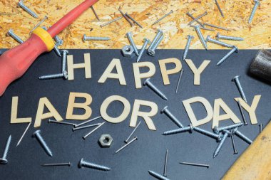 İşçi Bayramı 'nın anısına çivi ve çivilerle kaplı ahşap bir arka plan. Çekiç ve tornavidanın yanında tahta harfler var. Pankart.