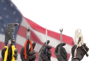 Güvenlik eldiveni takan işçilerin elleri odaklı olmayan bir ABD bayrağı önünde iş aletleri tutuyor..