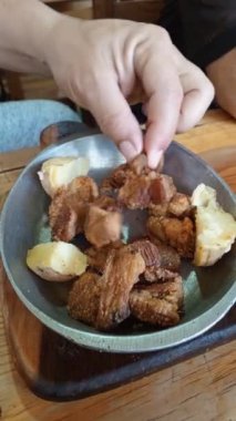 Tahta bir masadaki başlangıç tabağından chicharron toplayan bir el. Tipik Latin Amerika yemeği. Domuz eti çatırdıyor.