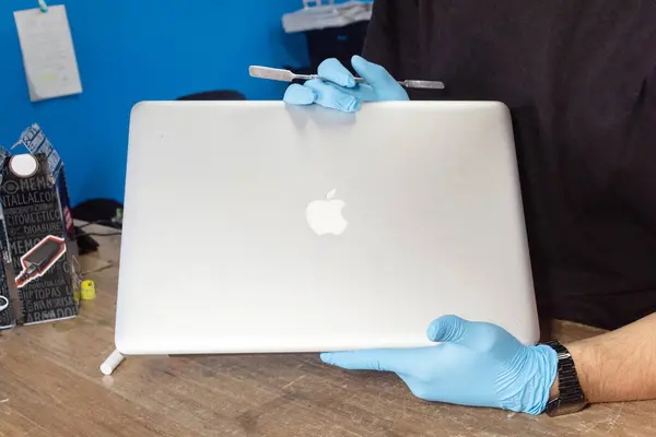 Bogota, Kolombiya - 25 Haziran 2024: Elma laptopu tutan koruyucu eldiven giyen bilgisayar tamircisi. Logo. Bilgisayar onarımı ve satış kavramı.