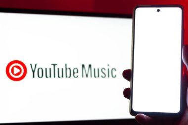 Bogota, Kolombiya - 12 Temmuz 2024: Ön planda boş ekran olan bir cep telefonu ve arka planda biraz bulanık YouTube müzik logosu olan bir laptop ekranı. Müzik yayın platformu.