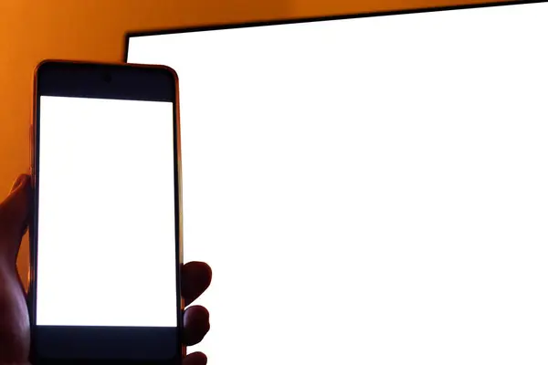 Ön planda boş bir ekran olan akıllı bir telefonu boş bir TV ekranının önünde tutmak..