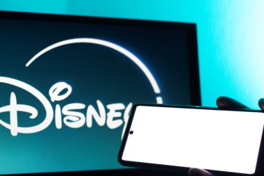 Bogota, Kolombiya - 12 Temmuz 2024: Disney Plus logosu olan bir televizyon ekranının önünde yatay pozisyonda cep telefonu tutan bir el. Tüm aile için akış. Ana ekran.