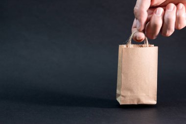 Siyah arka planda küçük bir kese kağıdını tutan bir el. Kopyalama alanı olan resim. Alışveriş konsepti.