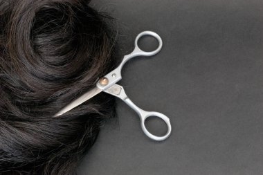 Profesyonel kuaför makası gri bir arka planda doğal siyah saç buklesiyle birbirine dolanmış. Güzellik konsepti. Tarz değişikliği.