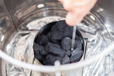 Sigara fıçısının içinde daha iyi dağıtmak için el çırpmak. Tütsüleme fıçısında yanma için bile kömür ayarlanıyor.