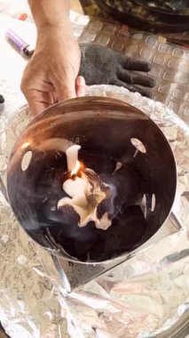 Bir insan, yanan bir varilin içindeki bir kağıt parçasını ateşe vermek için mum kullanır..