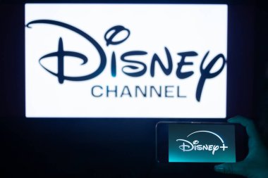 Bogota, Kolombiya - 14 Ocak 2025: Disney Channel logosu logosu logosu logoda loş bir televizyon ve ön planda Disney Plus logosu olan bir cep telefonuna vurgulandı